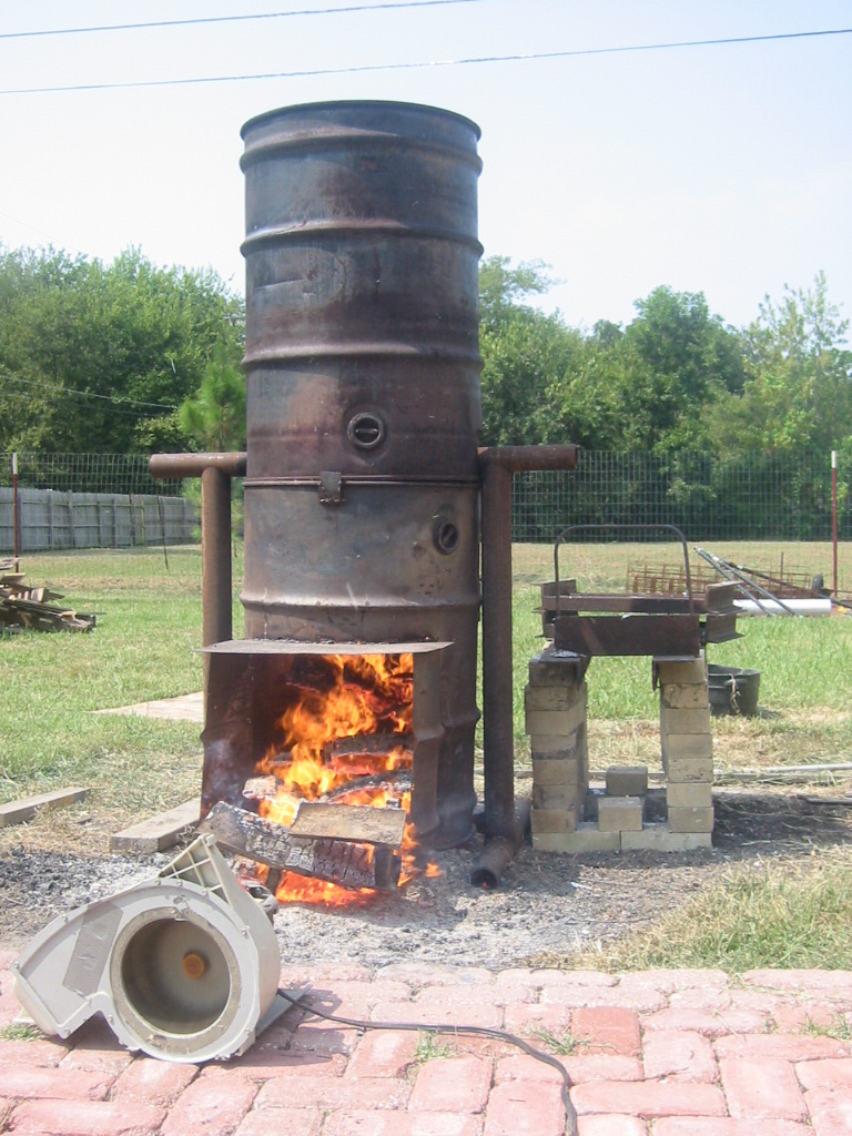 A blower removed from a clothes dryer fans the flames. A second barrel acts as a chimney to draw the heat past the pot.