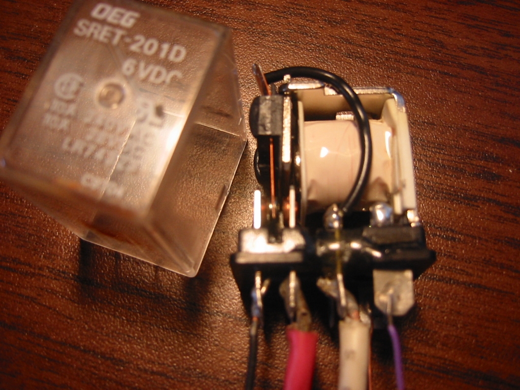 DPDT Relay with the cover removed showing the magnetic coil wrapped in white plastic and the contacts on the left side.